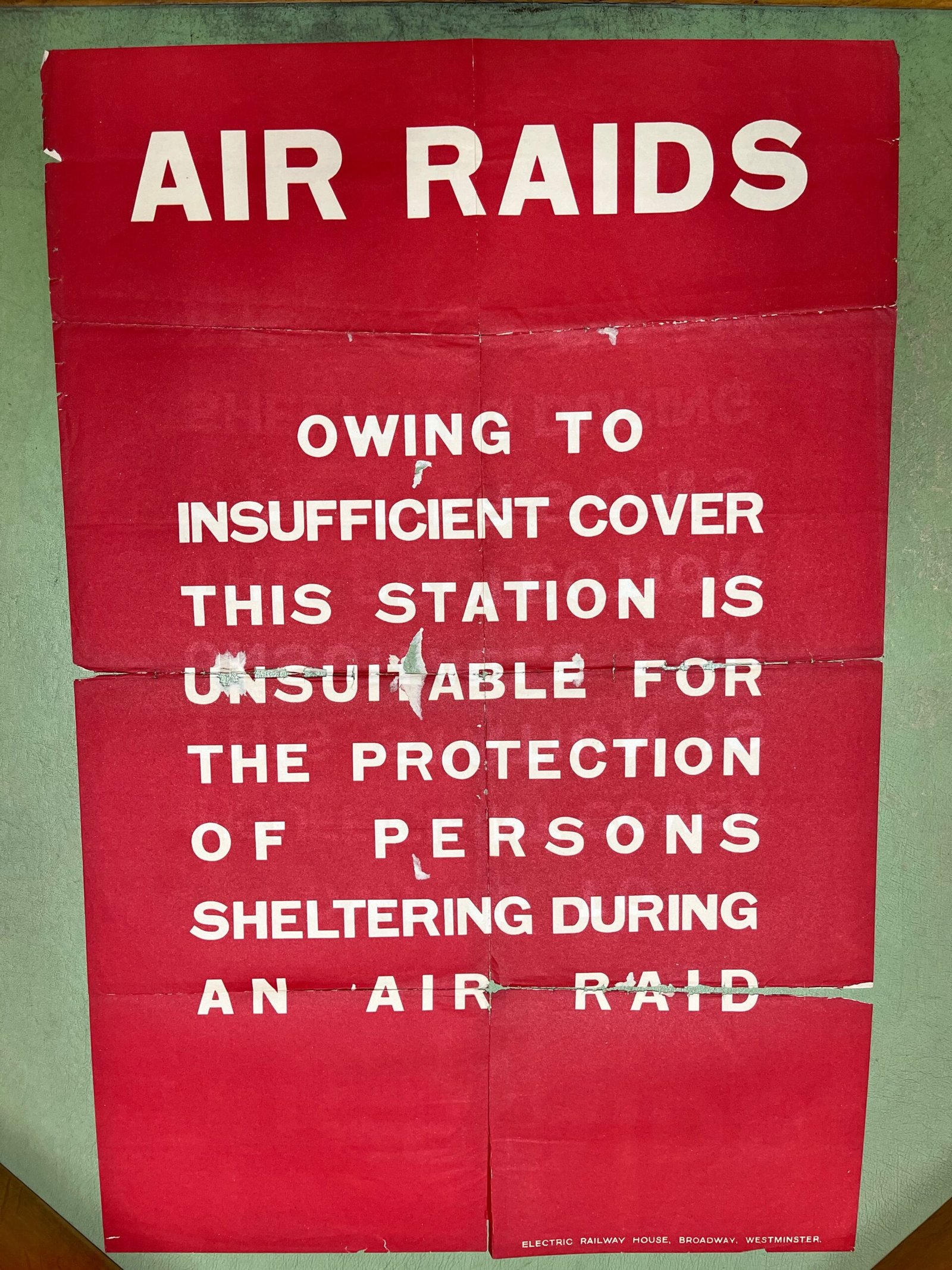 A printed sheet of paper with white text on a red background. The text reads: "AIR RAIDS OWING TO INSUFFICIENT COVER THIS STATION IS UNSUITABLE FOR THE PROTECTION OF PERSONS SHELTERING DURING AN AIR RAID"