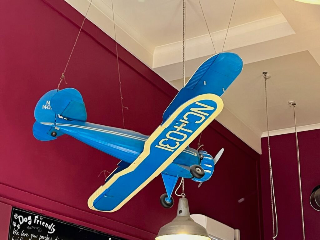 Model blue and yellow biplane with "NC14031" suspended from the ceiling in a room with cranberry-red walls.