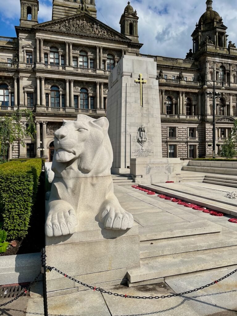 Large stone lion statue in front of a tall monument with a golden cross, set against an ornate historic building.