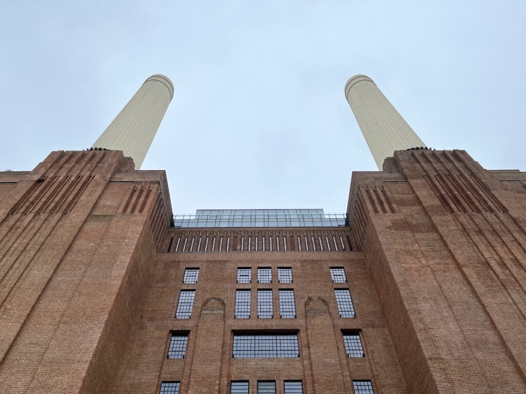 Upward view of a large brick industrial building with two tall white chimneys and rectangular windows.