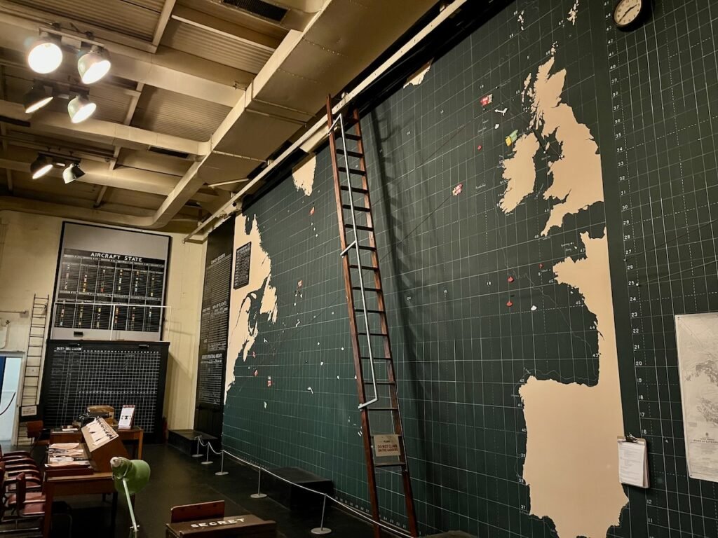 A historical military operations room with vintage equipment and a large wall map of the Northern Atlantic region.