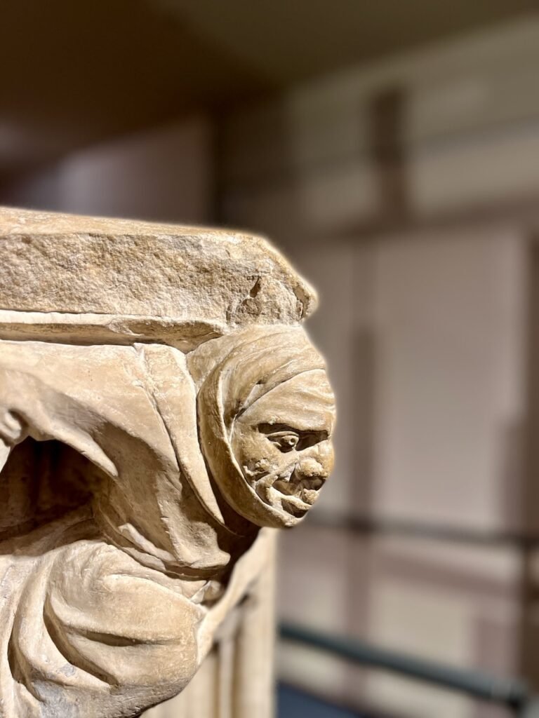 Close-up of a stone sculpture of a hooded figure with detailed facial and garment textures.