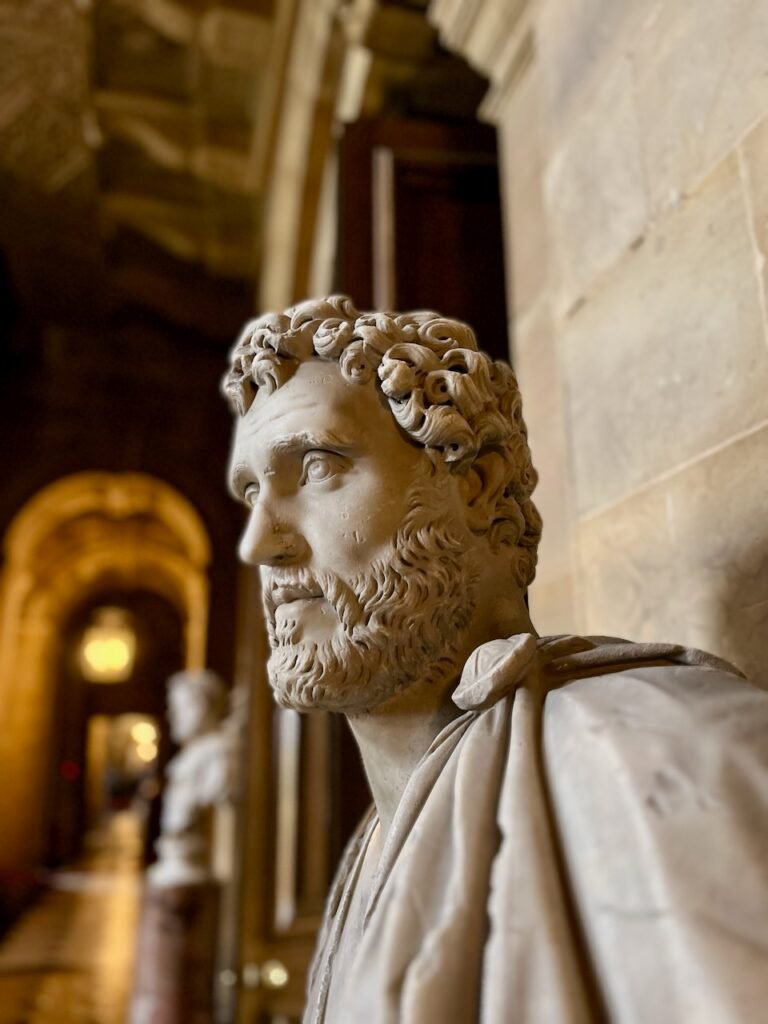 Stone bust of a bearded man in an ornate hallway with an arched ceiling and another bust in the background.