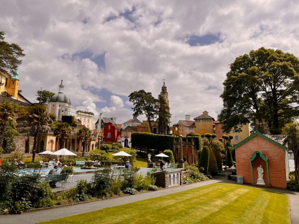 Colorful village scene with diverse architecture, green lawns, and a few tall trees under a cloudy sky.