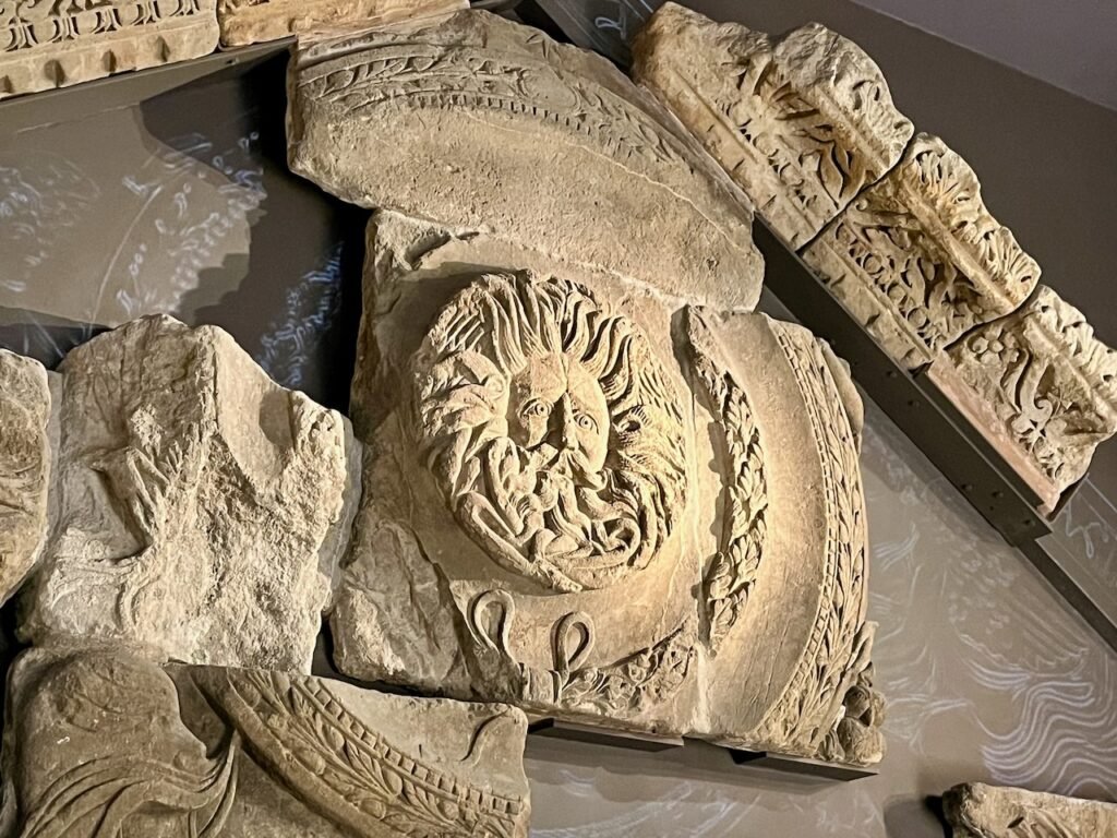 Ancient stone carvings featuring a relief of a face with snakes for hair at the centre, surrounded by decorative patterns.