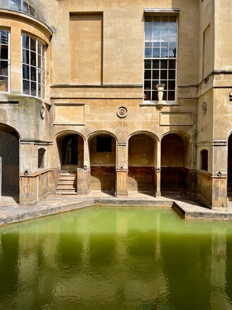 Stone pool with green water and arched structures, featuring large windows above.