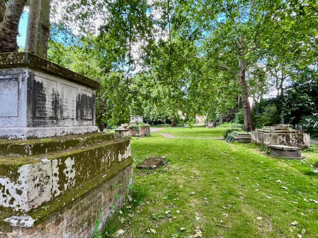 Stone tombs and leafy trees in a tranquil park setting.