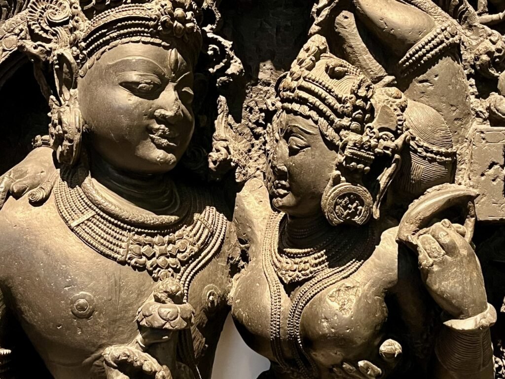 A detailed stone carving of a male and female figure adorned with elaborate headpieces and jewellery.