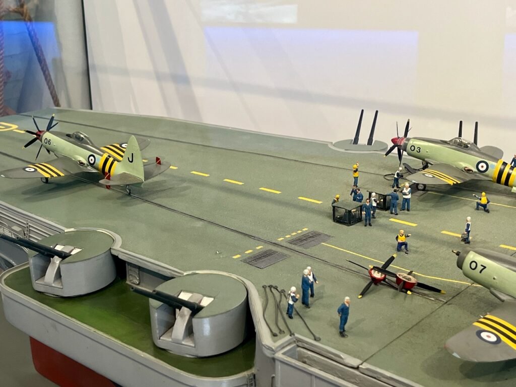 Model of an aircraft carrier deck with fighter planes and crew figurines.