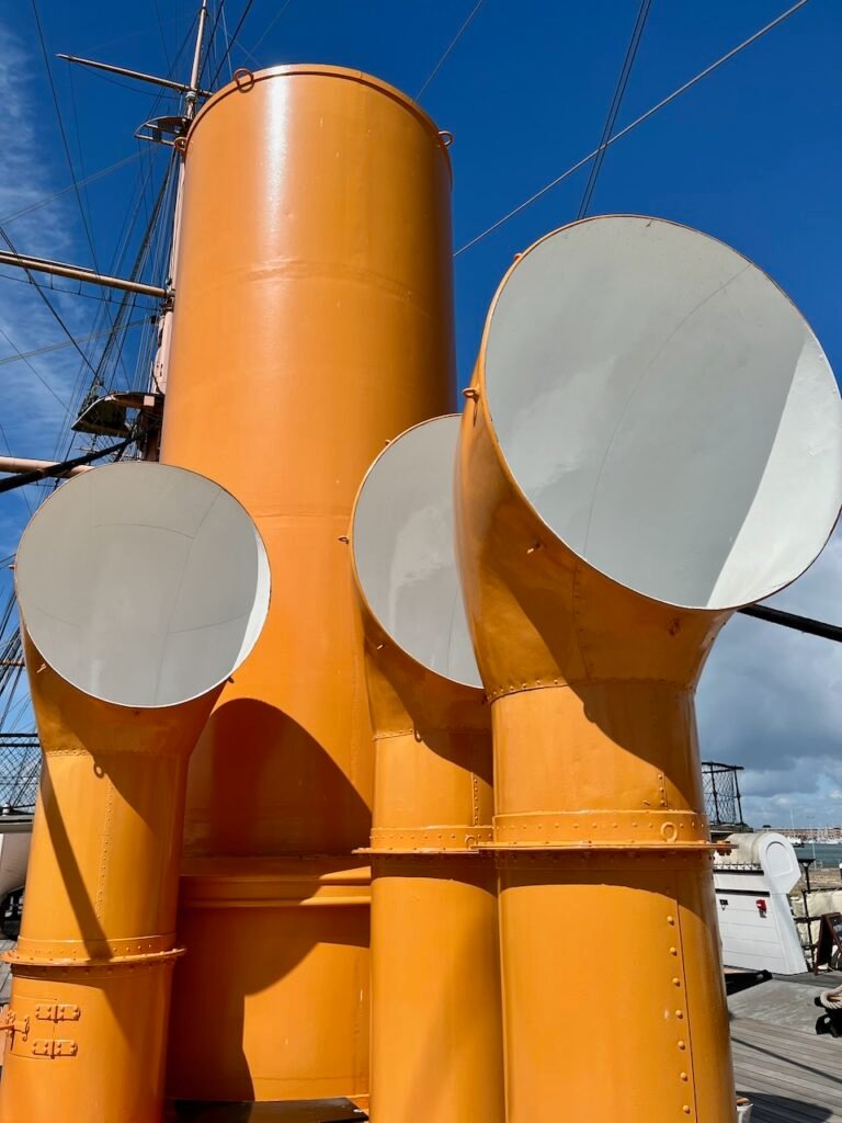 Bright orange ventilators of a historic ship against a blue sky.