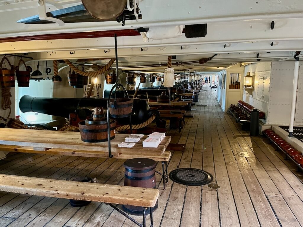 Interior view of a naval ship's gun deck with cannons and wooden benches.