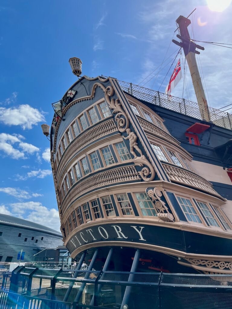 The stern of an old sailing ship, with three decks of elaborately decorated windows above the name "VICTORY".