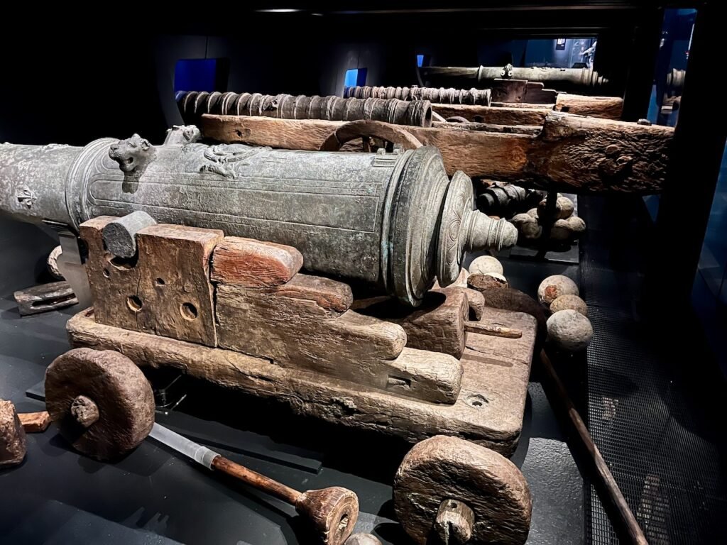 Exhibit of historical cannons on wooden carriages, displayed in a dimly lit museum.