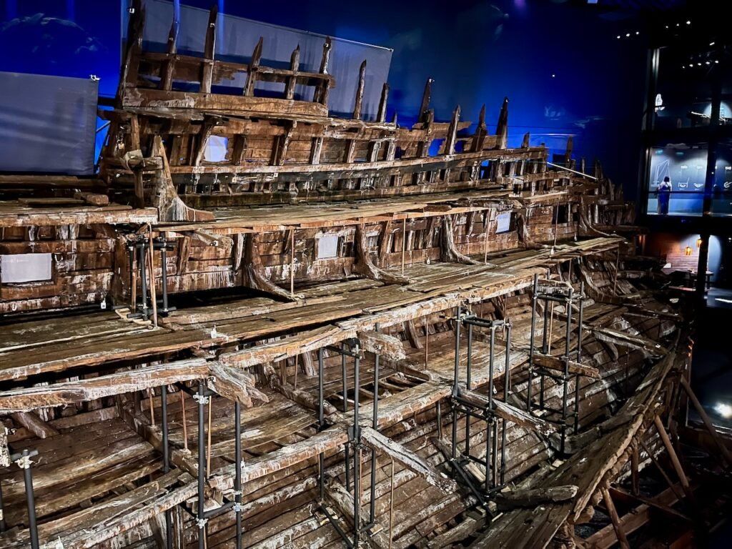 The interior of a very old wooden ship, supported by scaffolding and bathed in a dim blue light.